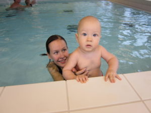 Pieni lapsi aikuisen kanssa uima-altaan reunalla.