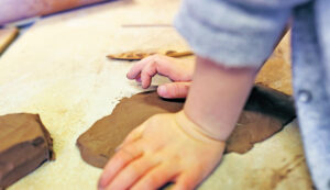 Lapsen kädet muotoilemassa savesta kuviota.