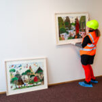 Marjo Heino ripustamassa Markku Arantilan akvarelliteoksia seinälle.