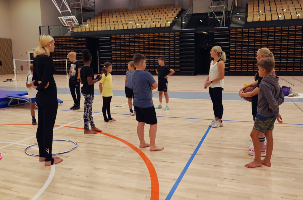 Lapsia kuuntelemassa ohjaajan ohjeistusta liikuntasalissa.