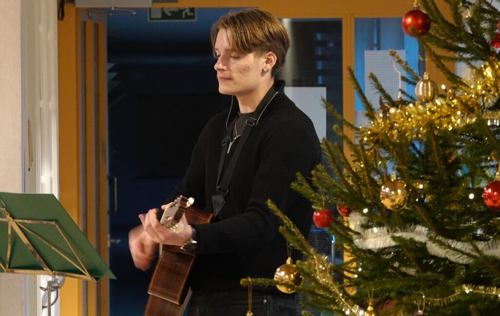 Soittaja kitaran kanssa joulukuusen vieressä.