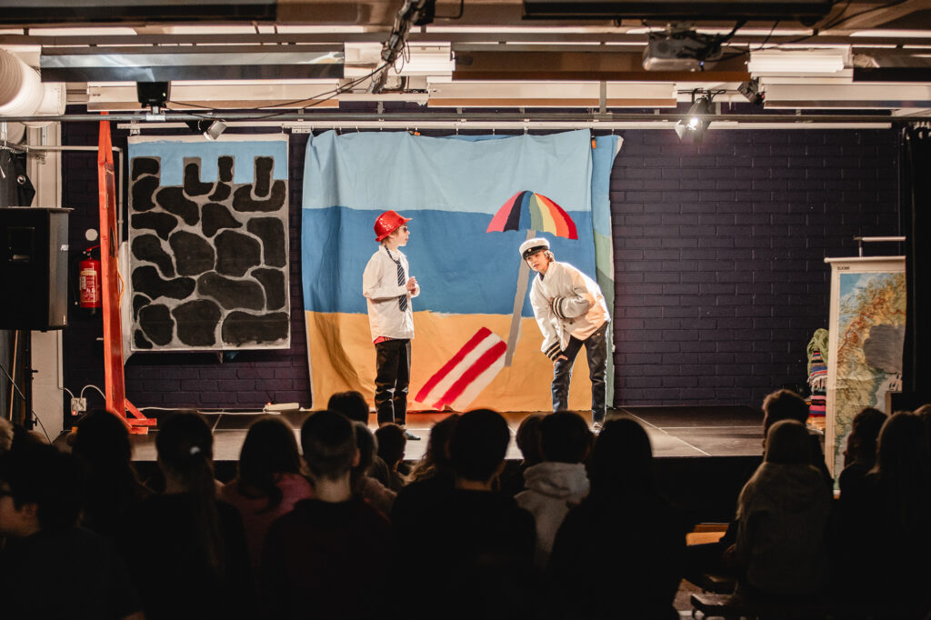 Two children standing in front of a canvas representing a beach. 