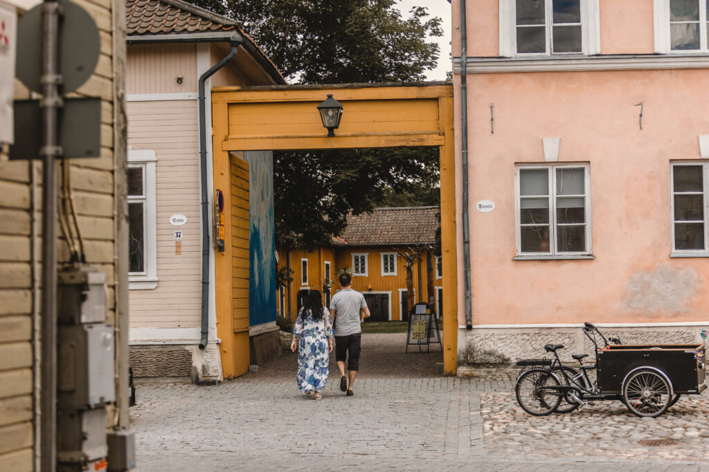 Taidemuseon sisäpihalle vievä portti, joka on pienemmän puurakennuksen ja isomman kivirakennuksen välissä. Kaksi aikuista on astumassa portista siäpihalle. Puutalon seinässä näkyy sininen seinämaalaus.