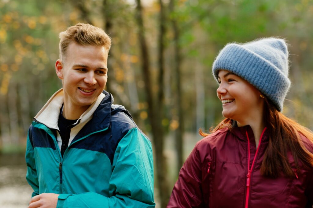 A smiling man and woman standing side by side in the middle of a forest.